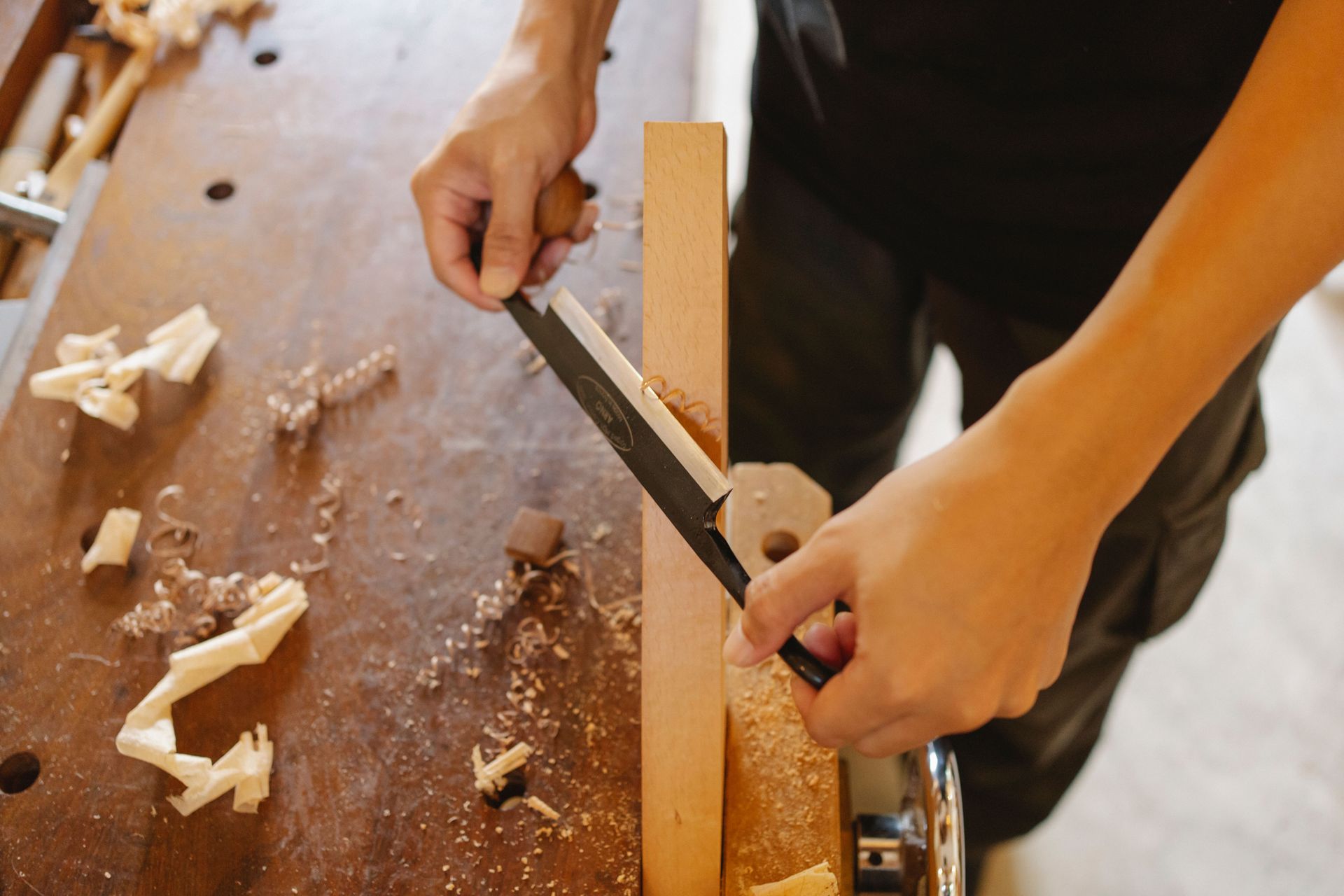 From above of crop anonymous craftsman cutting wooden plank with sharp chisel during work in carpenter workshop